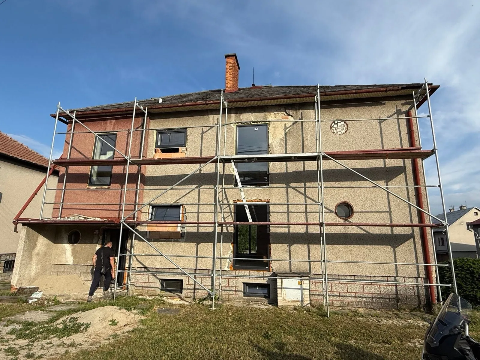 Rodinný dům před rekonstrukcí: lešení, poškozená omítka, rozpracovaná okna